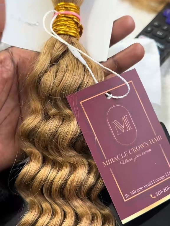 A bundle of honey blonde wavy hair with a burgundy Miracle Crown Hair tag reading Wear your crown